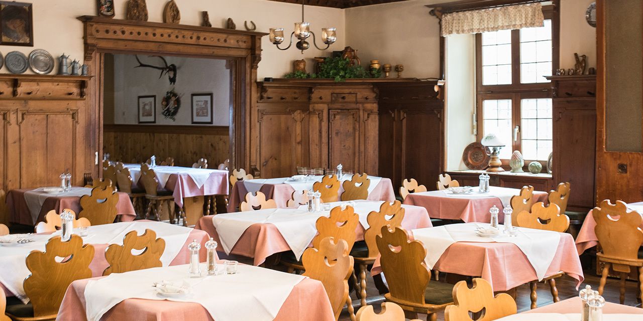 A dining room with multiple tables, each covered with a white tablecloth and surrounded by wooden chairs with carved designs.