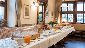A breakfast buffet setup with various food items and beverages, a checkered tablecloth, and a window view. - Hotel Zum Specht (Hoesbach)