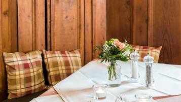 A wooden dining table set with white tablecloth, plaid pillows, and a floral centerpiece.