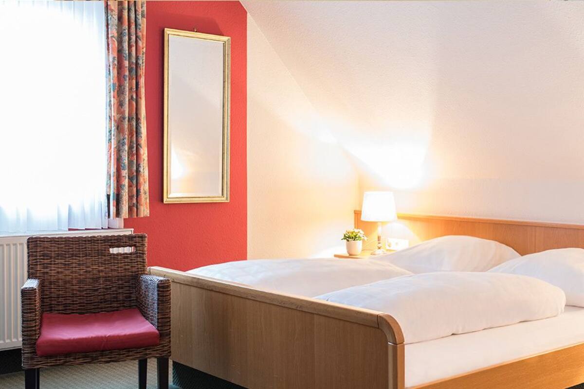Una camera d'albergo con un letto, una sedia, un comodino e uno specchio.