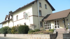 A two-story building with a beige facade, a tiled roof, and a sign indicating it is a guesthouse. - Hotel Zum Specht (Hoesbach)