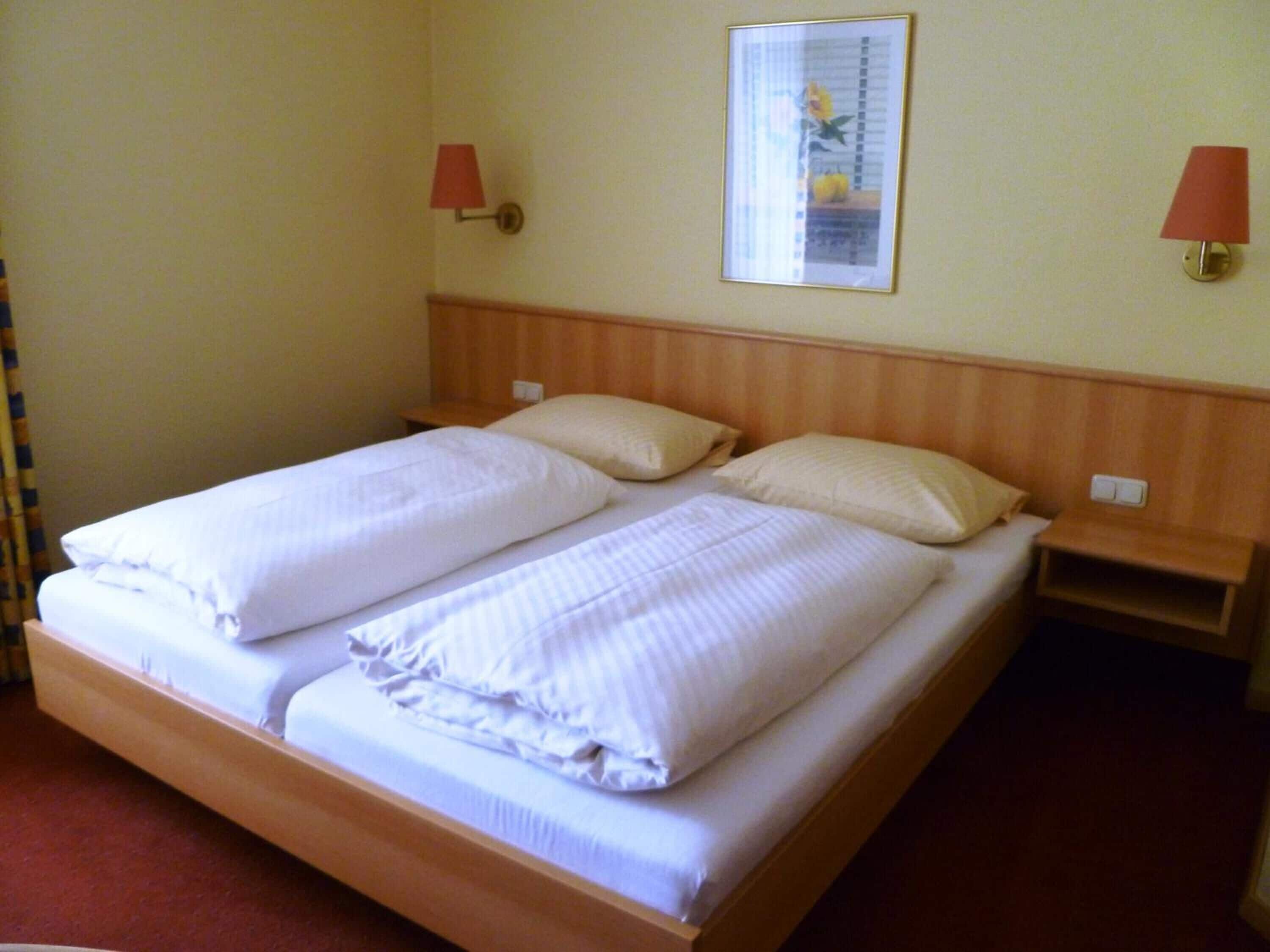 A double bed with white linens, two bedside tables, and a wall-mounted lamp.