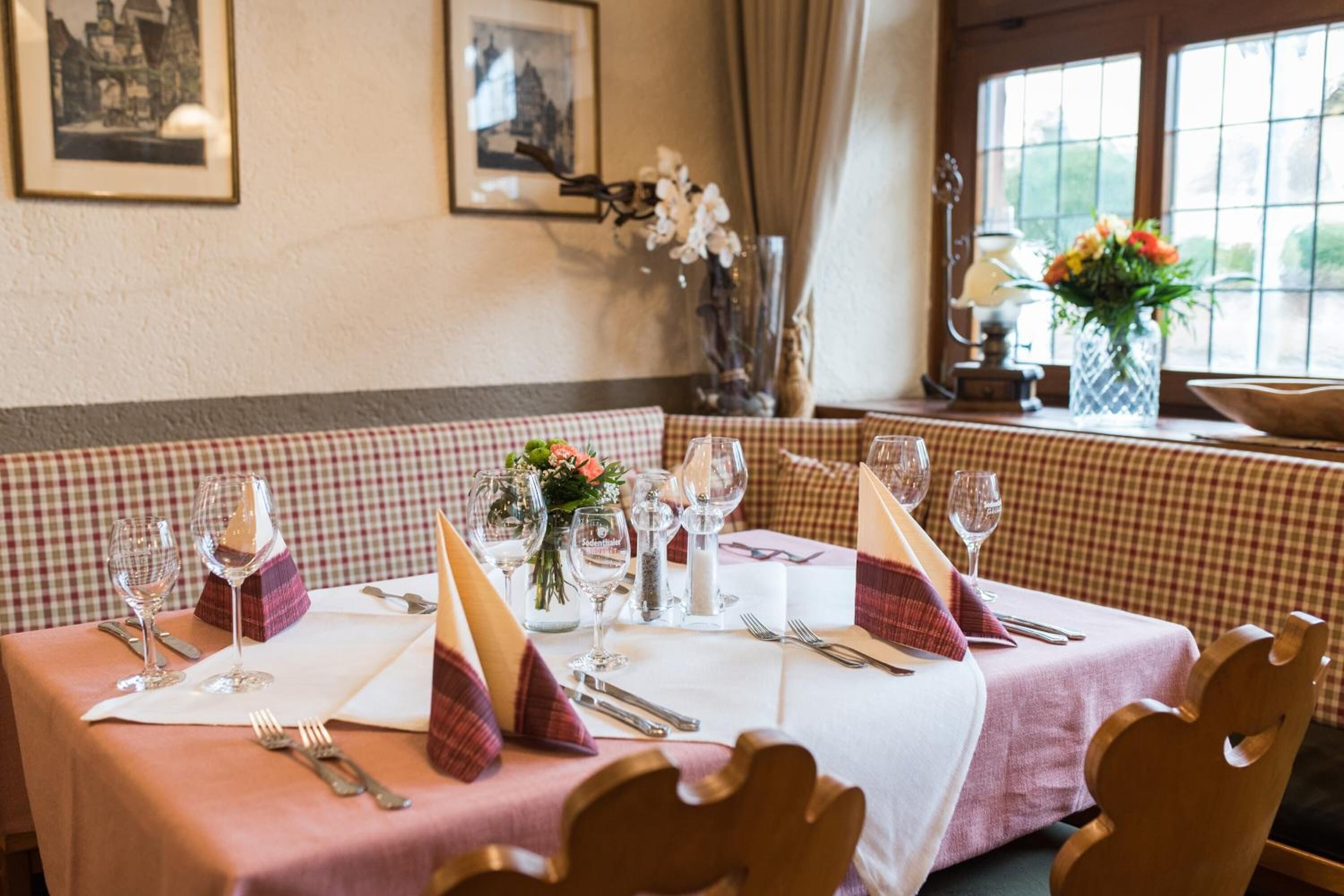Un espace repas avec des nappes à carreaux, des tables soigneusement dressées avec des verres à vin, des couverts et des centres de table floraux.