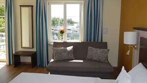 Een hotelkamer met een bed, een bank, een klein tafeltje, een spiegel, een lamp en een raam met gordijnen.