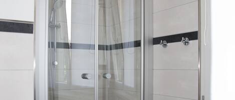 Un box de ducha con paredes de vidrio, una toalla blanca en el suelo, paredes de azulejos blancos y una banda horizontal negra.
