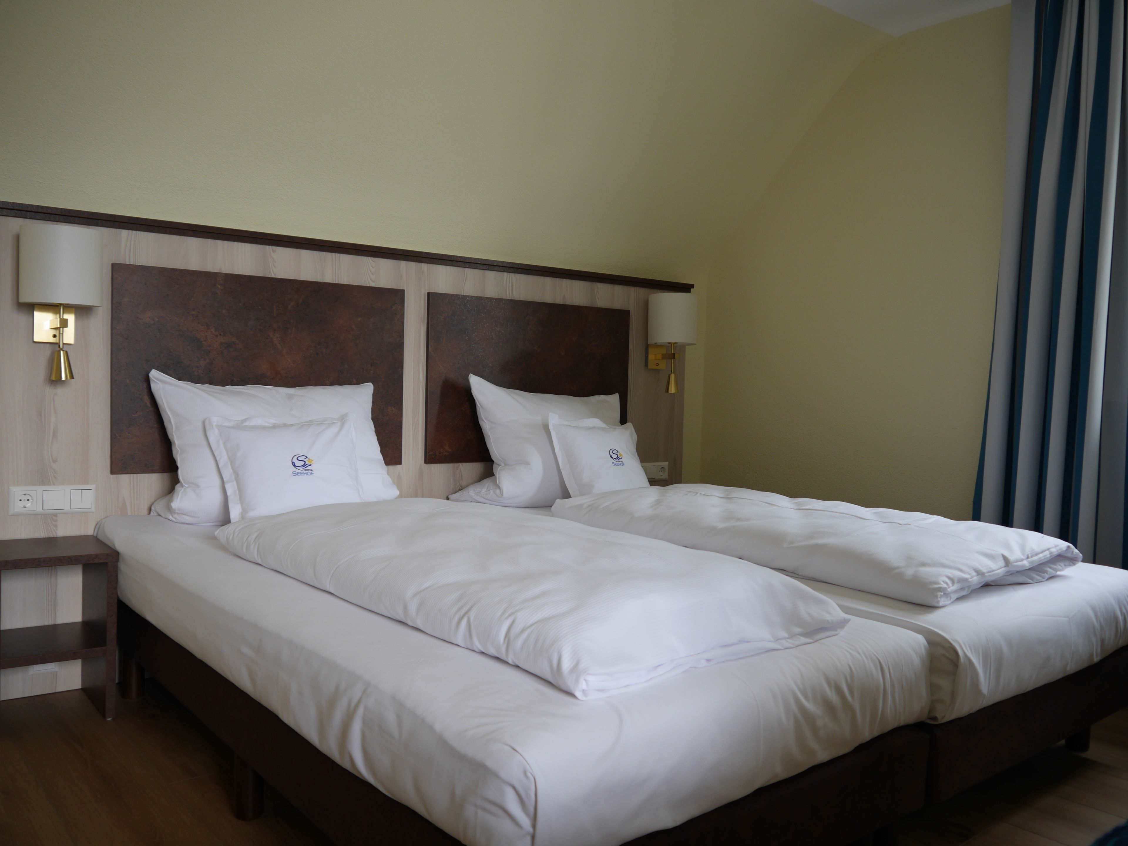 Cama doble con sábanas blancas, cabecera de madera, lámparas de noche y mesita de noche.
