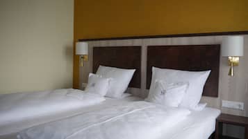 Ein Hotelzimmer mit zwei Einzelbetten, jeweils mit weißer Bettwäsche und Kissen, einem Holz-Kopfteil und Wandlampen.