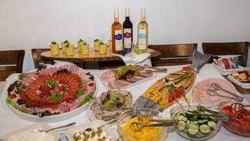 Un tavolo con buffet assortito, con un ampio vassoio di salumi, un pesce e diverse insalate. Si vedono anche bottiglie di vino sul tavolo.