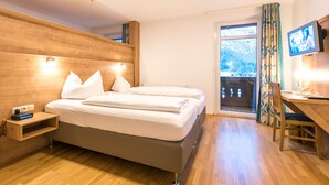 A bedroom with a wooden headboard, a bed with white linens, a bedside table with a clock, and a TV on the wall. - Almenrausch und Edelweiss (Garmisch-Partenkirchen)