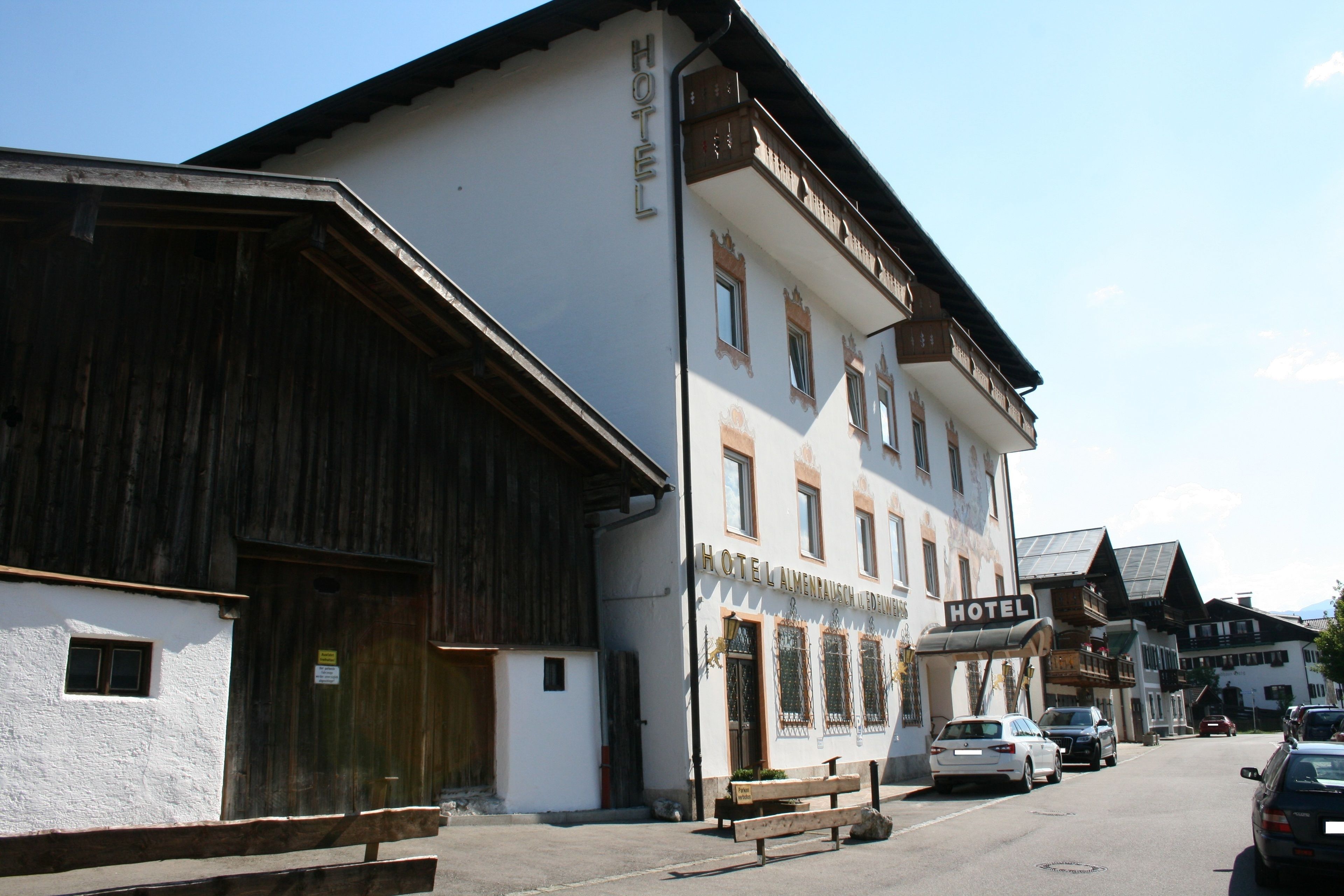 A traditional hotel with a white facade and wooden accents. It features a sign indicating it is a hotel, multiple windows, and a visible entrance.
