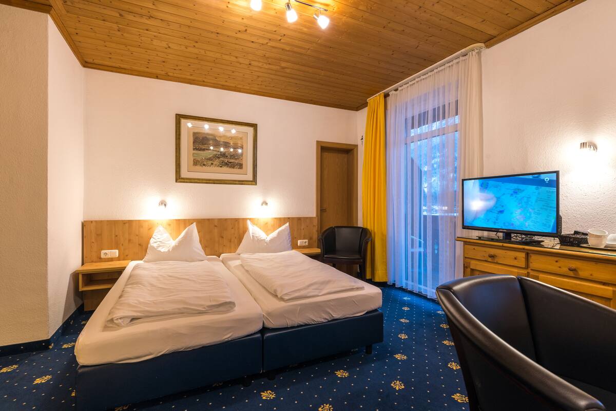 A hotel room with a double bed, a desk with a computer, a chair, a TV, and a framed picture on the wall.