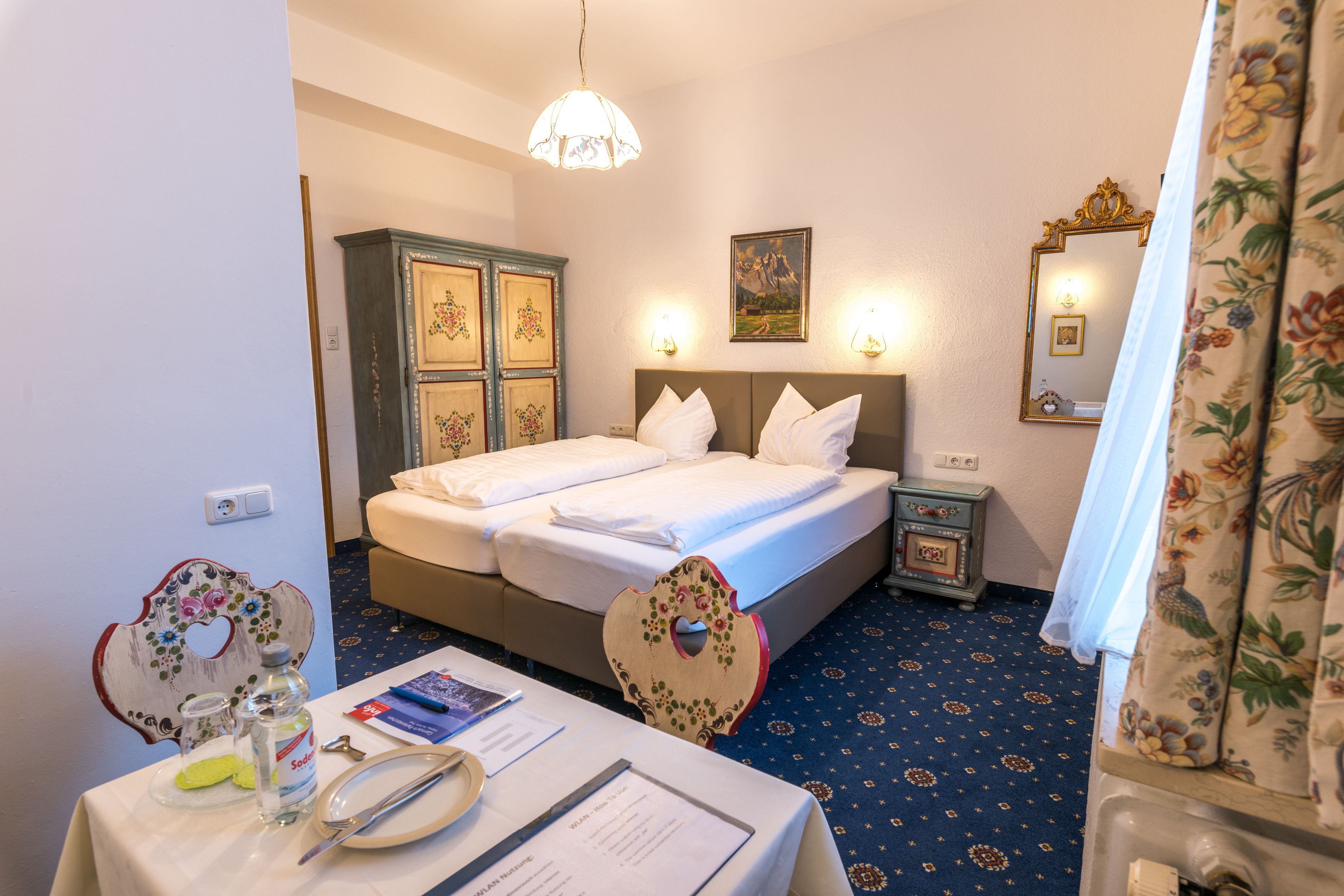 Una camera d'albergo con un letto rifatto, un comodino con una lampada, uno specchio e una tenda a motivi floreali.