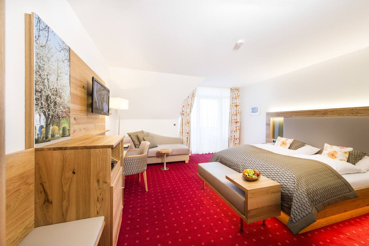 A hotel room with a bed, a desk, a chair, a small table, and a large window with curtains.