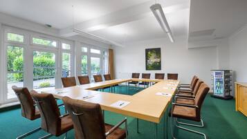 Ein Konferenzraum mit langem Tisch, braunen Stühlen, einem grünen Teppich und einem Automaten.