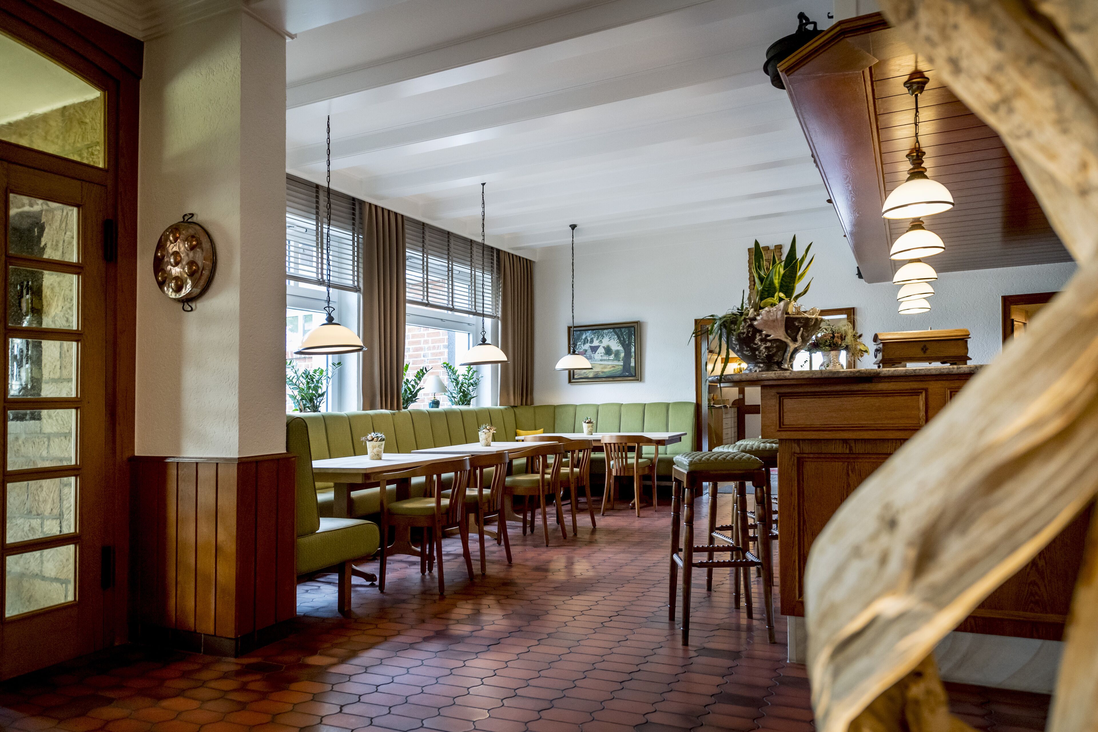 Ein Restaurant mit Holztischen, einem Backsteinboden und großen Fenstern.