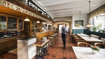 A restaurant with a bar area, wooden tables, and a waitstaff member.
