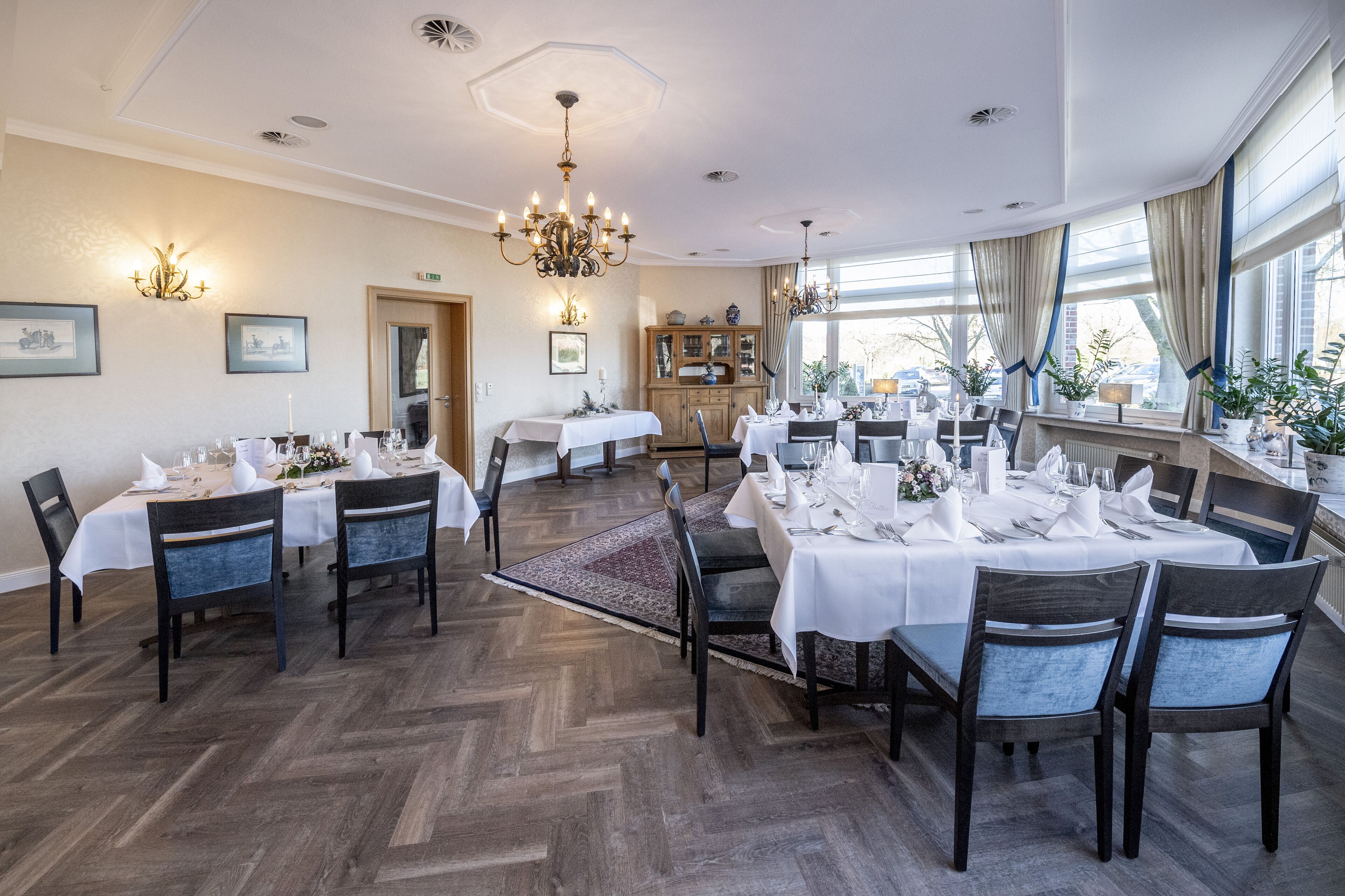 Un espace repas avec des tables rondes dressées pour le repas, un plancher en bois et un lustre.