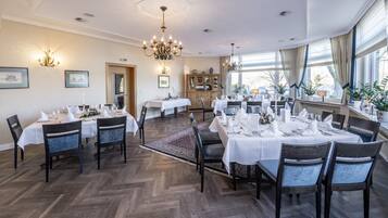 Un espace repas avec des tables rondes dressées pour le repas, un plancher en bois et un lustre.