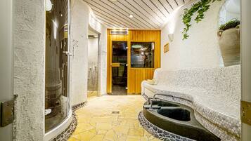 A spa area with a stone floor, a large bathtub, and a wooden door leading to another room.