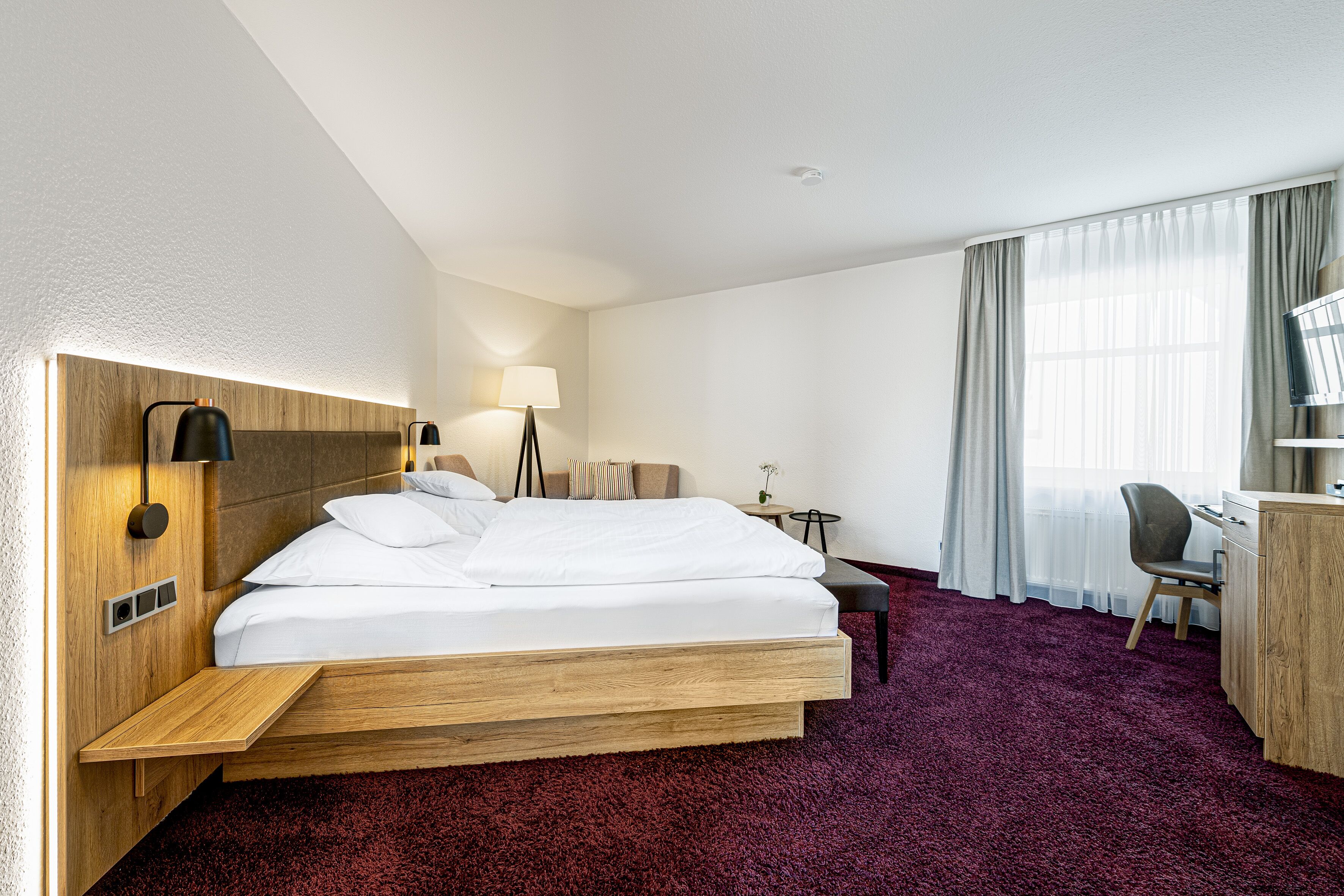 A hotel room with a bed, bedside tables, a desk, and a chair.