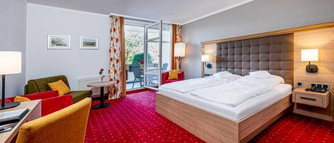 A hotel room with a large bed, a desk with a chair, a small table, and a red carpeted floor.