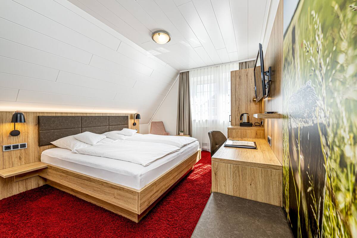 A modern hotel room with a wooden bed, a desk, and a large window with curtains.