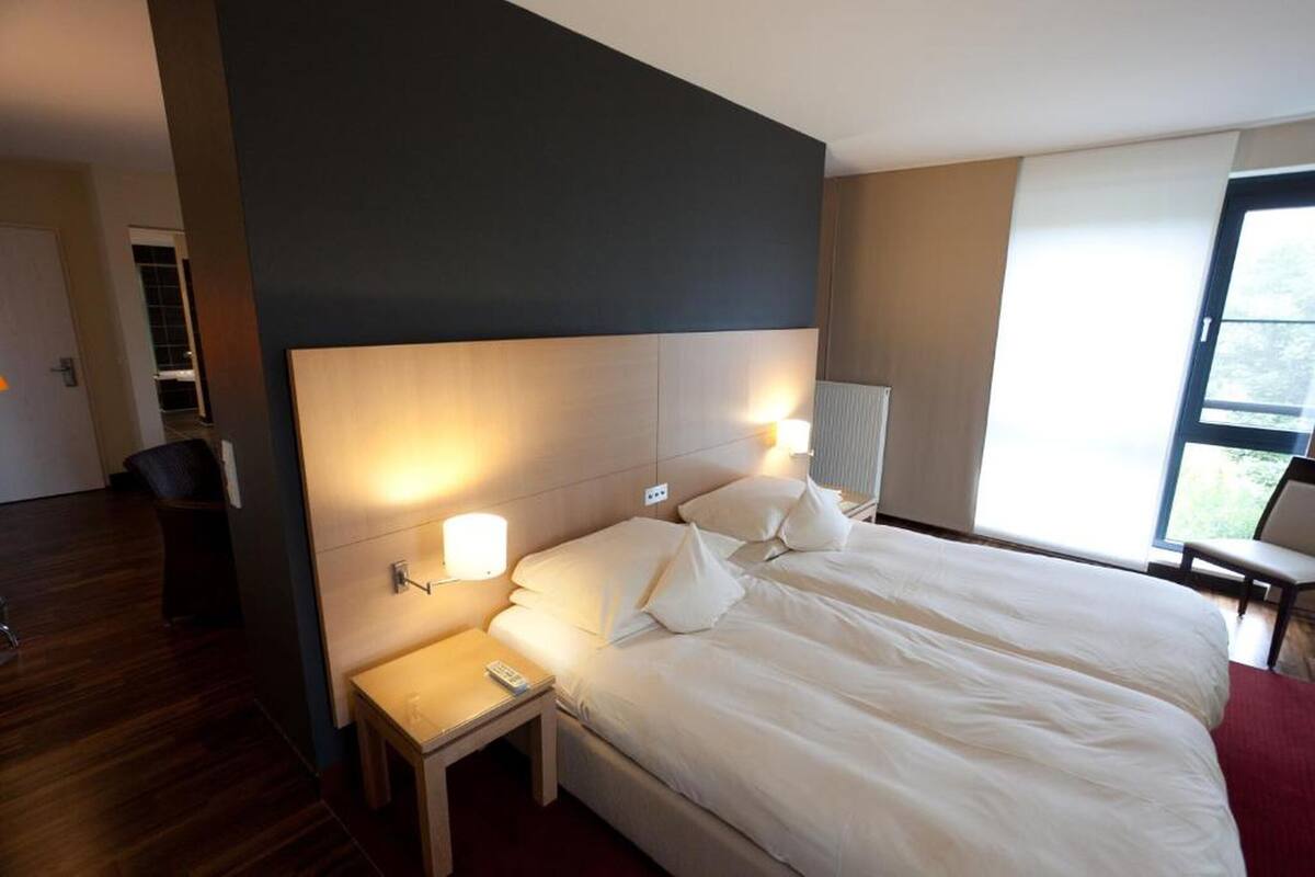Ein Hotelzimmer mit einem großen Bett, Nachttischlampen, einem kleinen Tisch und einem Fenster mit Blick.
