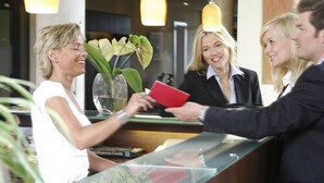 Un comptoir d’accueil avec un réceptionniste, un client et un membre du personnel de l’hôtel.