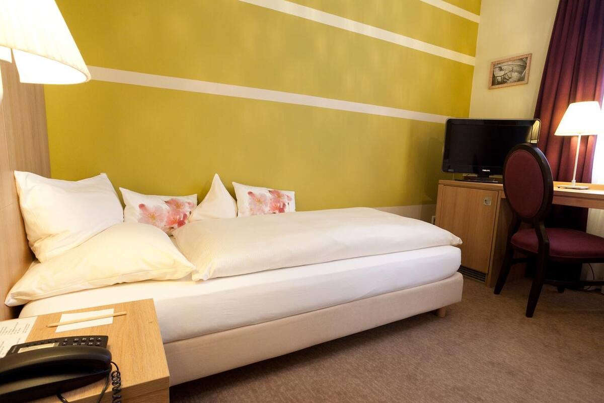 Ein Hotelzimmer mit Bett, Schreibtisch, Fernseher und Telefon.