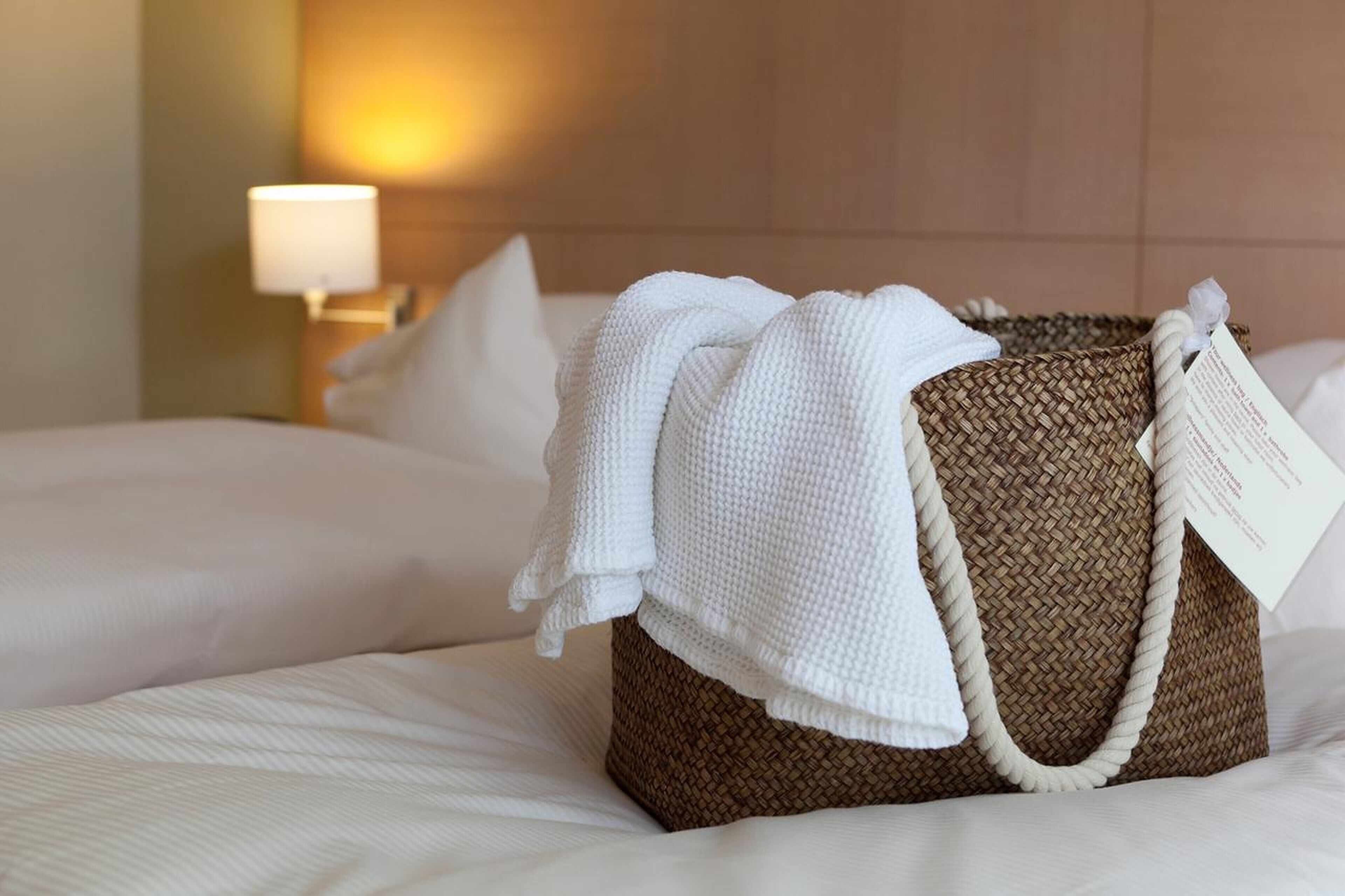 Una cesta de mimbre con una etiqueta sobre una cama en una habitación de hotel.