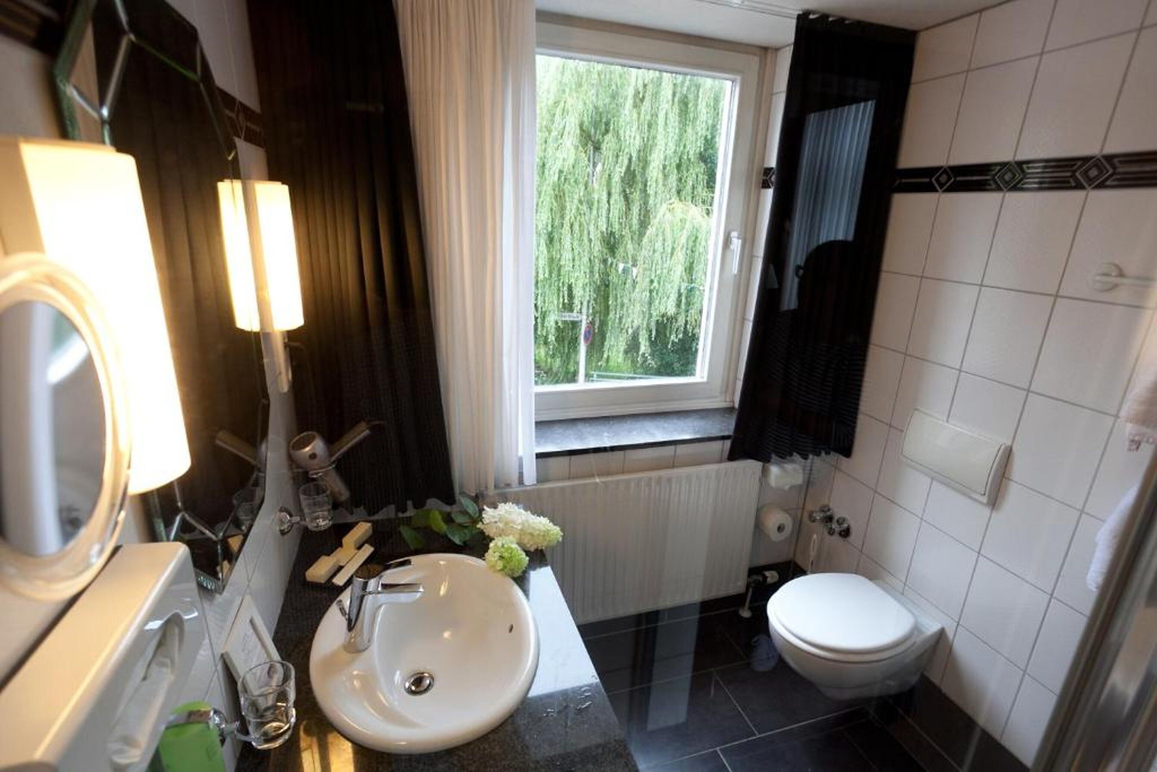 A bathroom with a white sink, a mirror, a window with a view of trees, a toilet, and a towel rack.