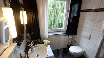 A bathroom with a white sink, a mirror, a window with a view of trees, a toilet, and a towel rack.