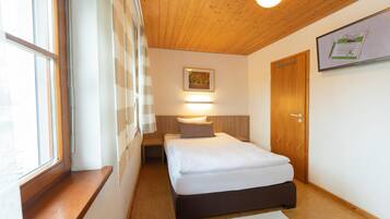 A bedroom with a wooden ceiling, a bed with white bedding, a nightstand, a window with blinds, and a door with a sign.