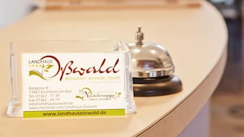 Ein Empfangstisch mit einer transparenten Vitrine, die eine Visitenkarte für 'Landhaus Osswald' und eine Klingel enthält.