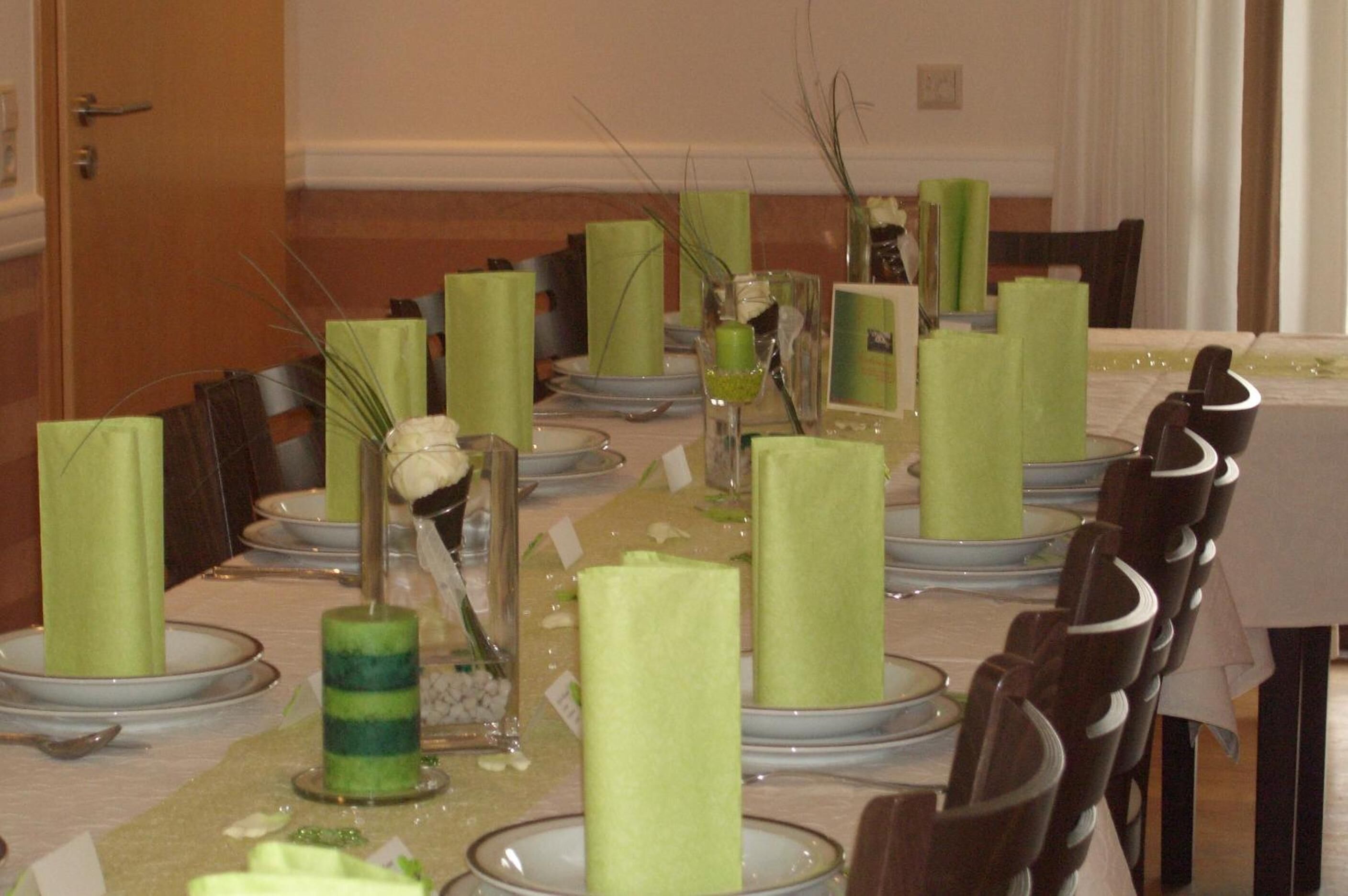 A dining table set with green napkins, clear glass vases with greenery, and a decorative centerpiece.
