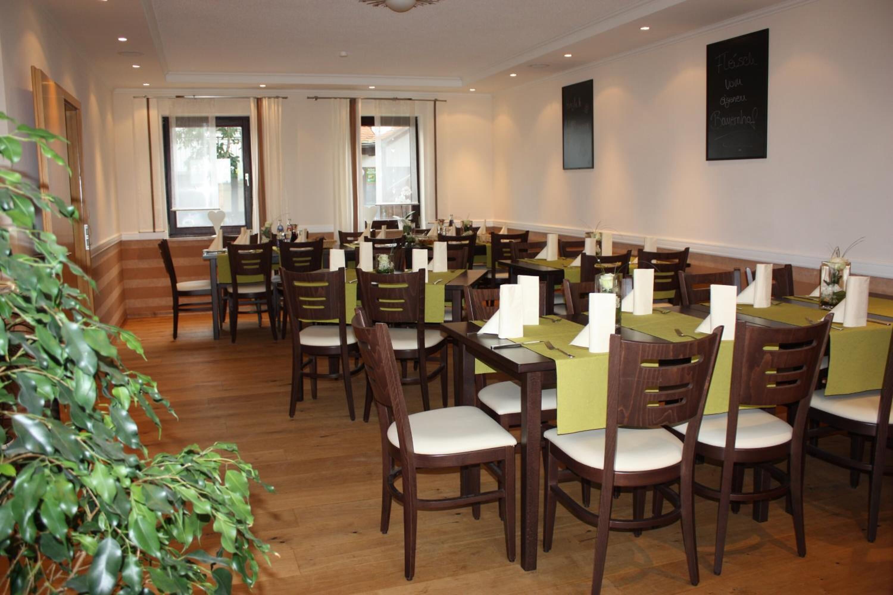 Un comedor con varias mesas y sillas, un ventanal grande y una planta al frente.