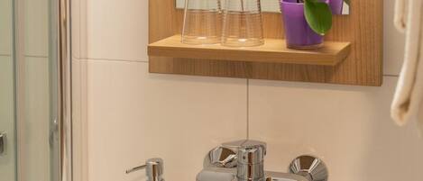 A bathroom with a white sink, a mirror, and a shelf with glass bottles and a potted orchid.