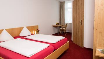 A hotel room with two beds, a wooden desk, a chair, and a door.