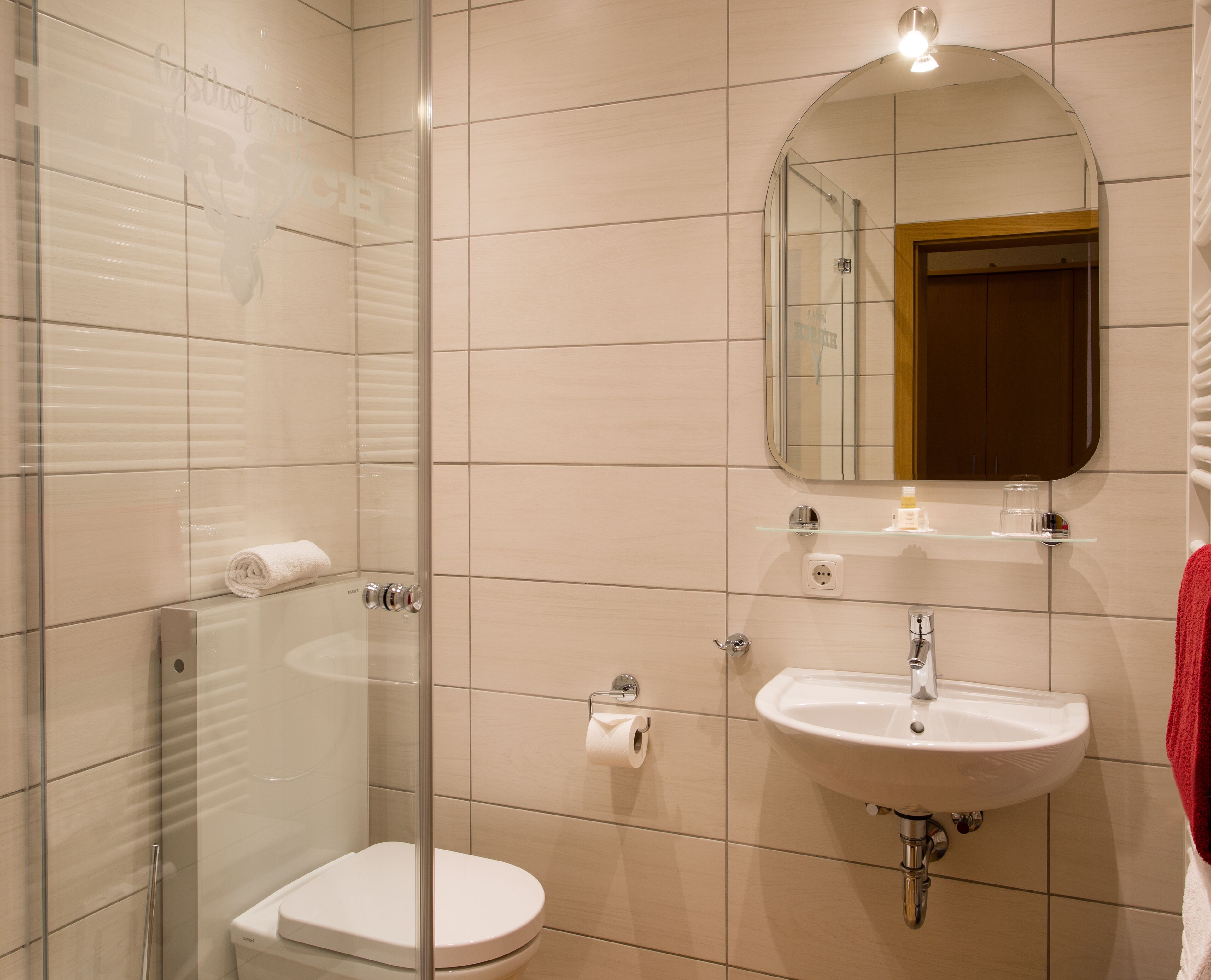 Un baño moderno con cabina de ducha de vidrio, un inodoro blanco, un lavabo con espejo y un perchero para toallas.