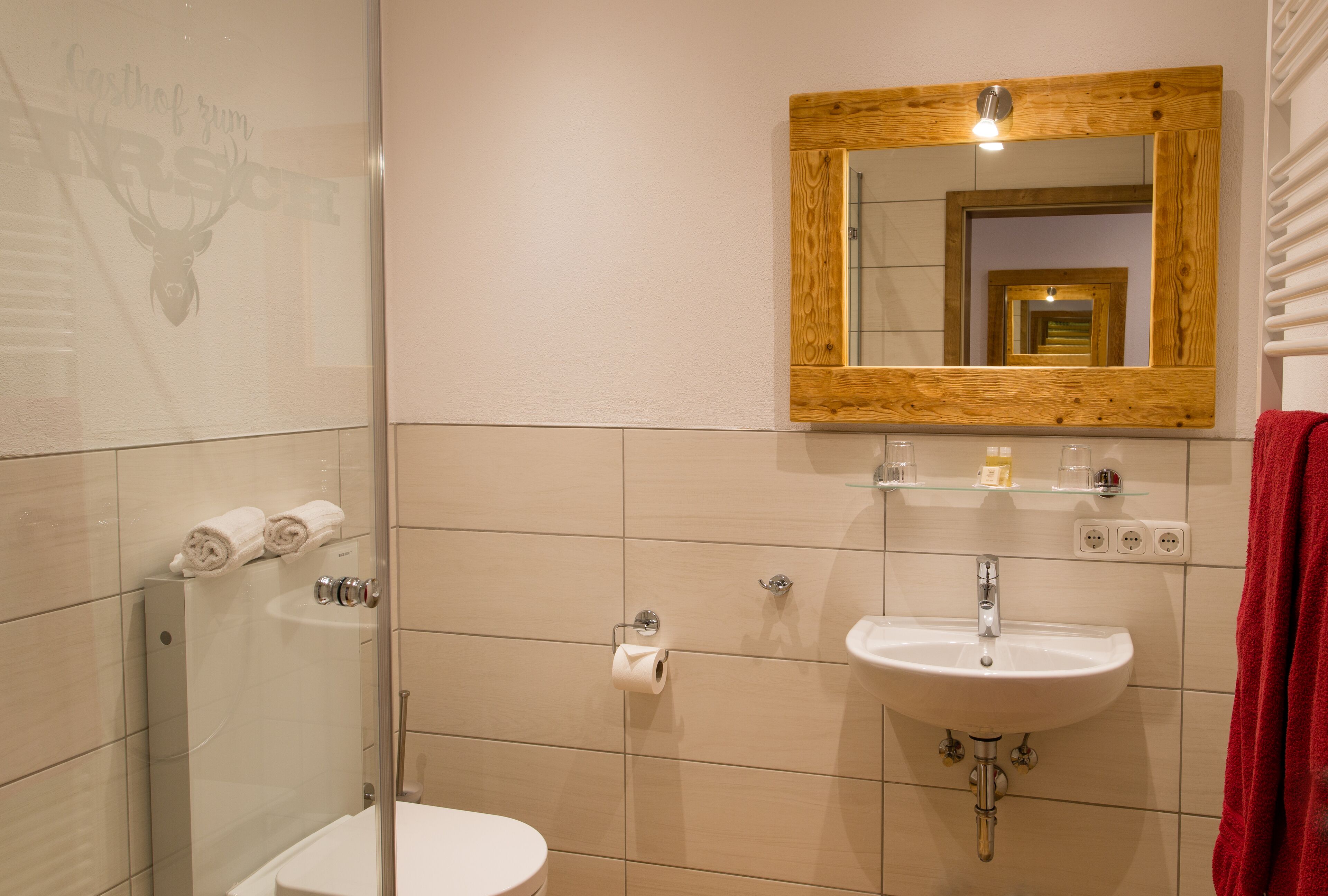 Un baño con cabina de ducha de vidrio, lavabo blanco y espejo con marco de madera.