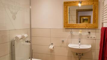 Un baño con cabina de ducha de vidrio, lavabo blanco y espejo con marco de madera.