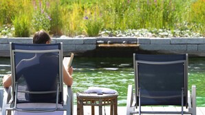 Deux chaises sont placées face à un plan d’eau, avec un jardin en arrière-plan.