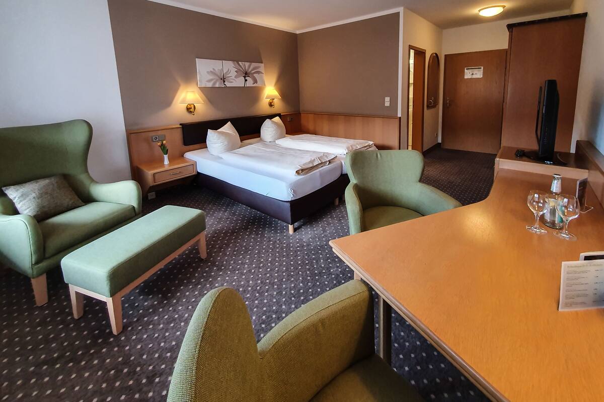 Une chambre d’hôtel avec un lit, deux fauteuils, une petite table et un téléviseur.