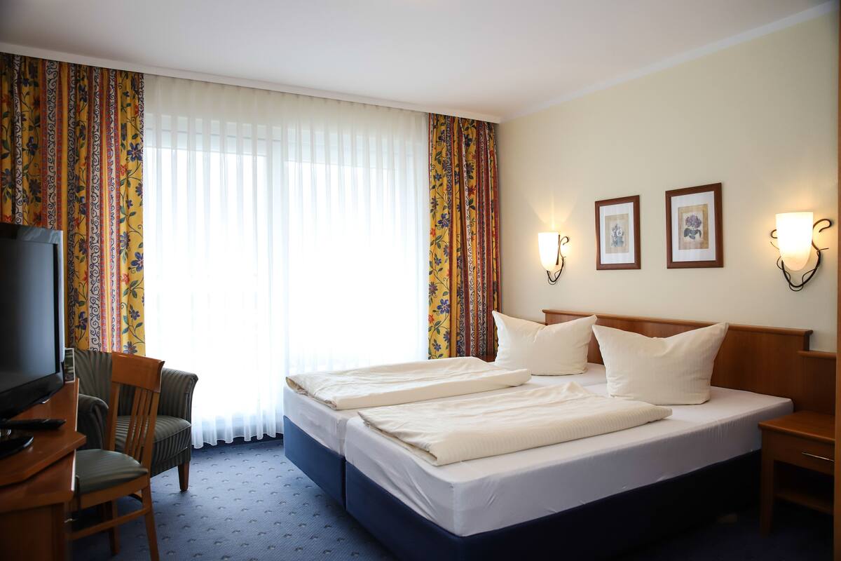 Une chambre d’hôtel avec un grand lit, deux tables de chevet, une télévision, une chaise et des rideaux.