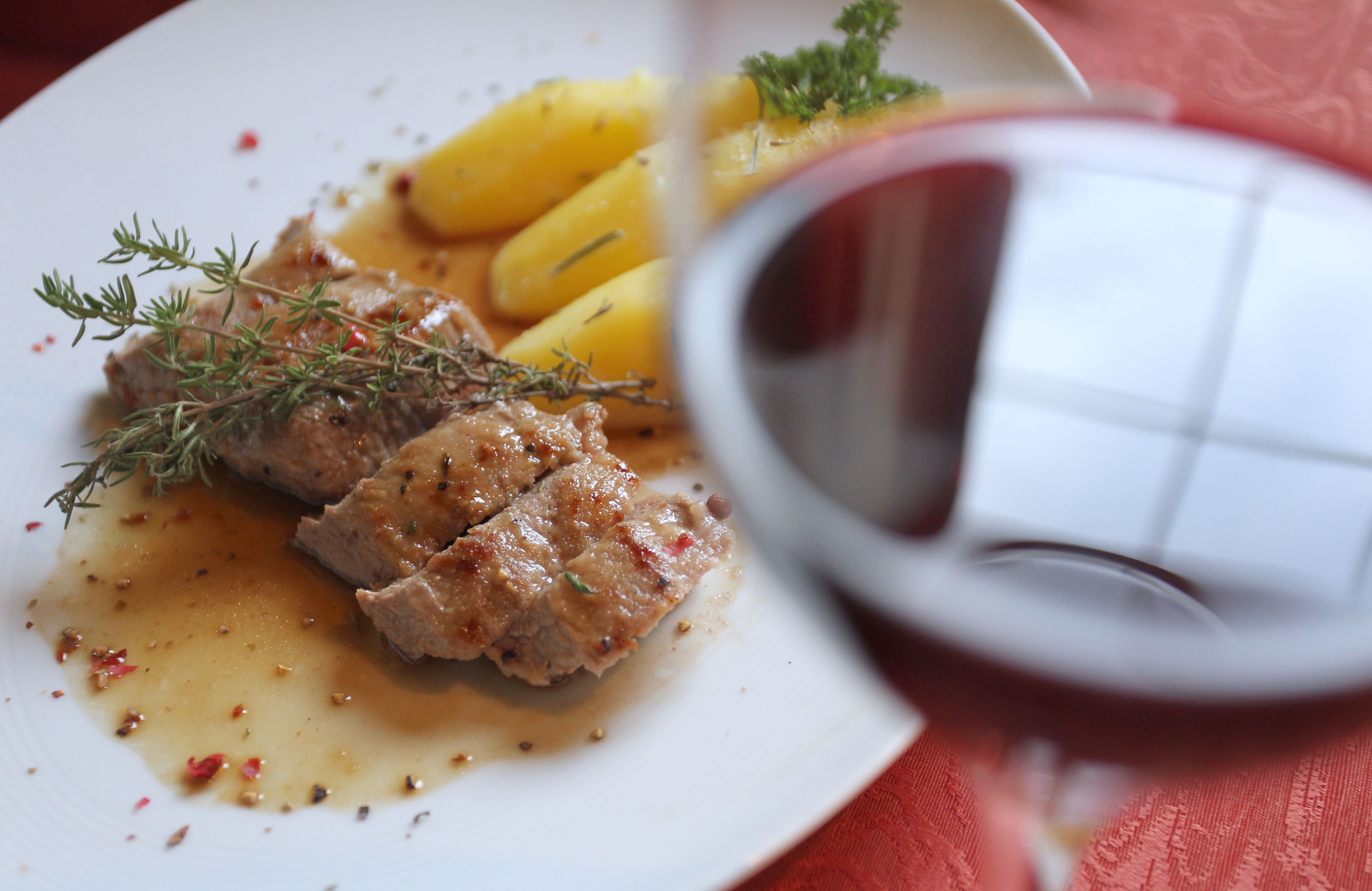 A plate of food with meat, potatoes, and a sprig of thyme.