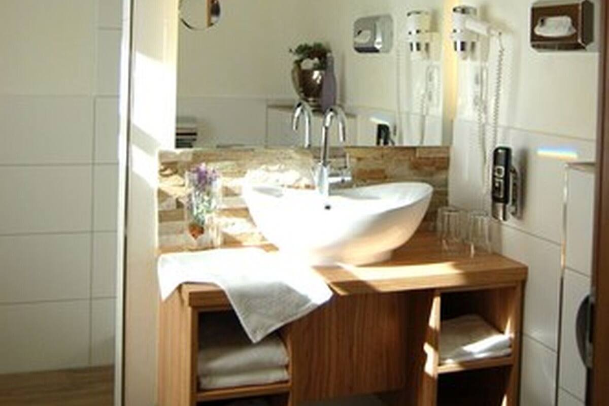 A modern bathroom with a wooden vanity, a large mirror, a white sink, and a towel rack.