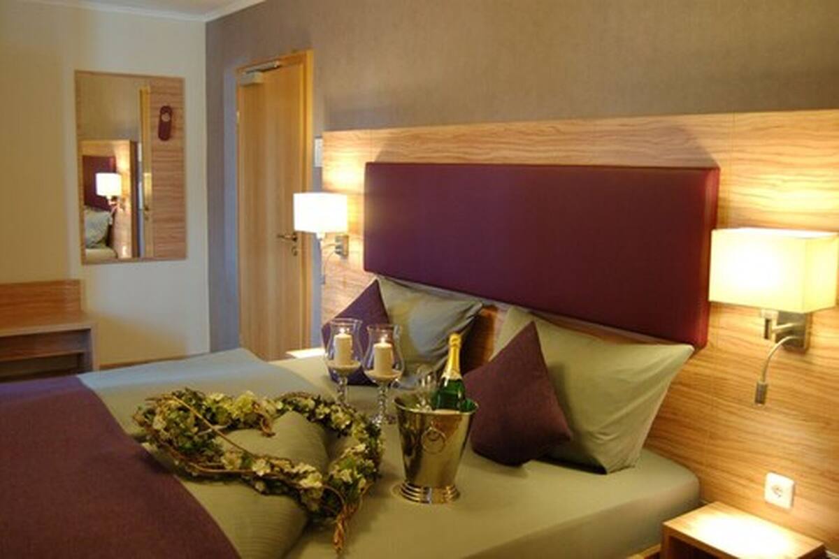 A hotel room with a bed, a nightstand, a mirror, and a wall-mounted lamp.