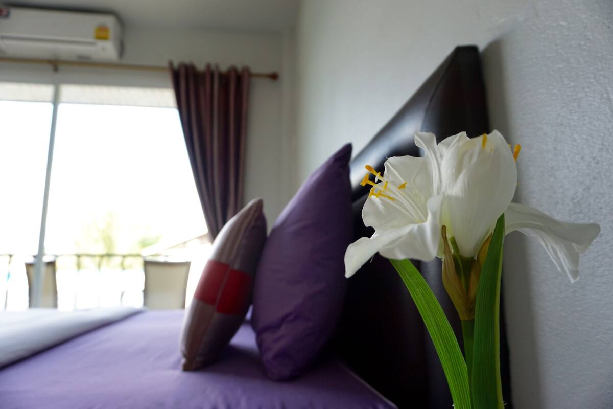 A hotel room with a bed, purple pillows, and a white flower.