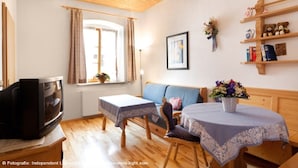 A cozy living room with a television, a sofa, a small table, and a window with curtains.