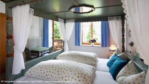 A bedroom with a canopy bed, a small table, and a window with curtains.